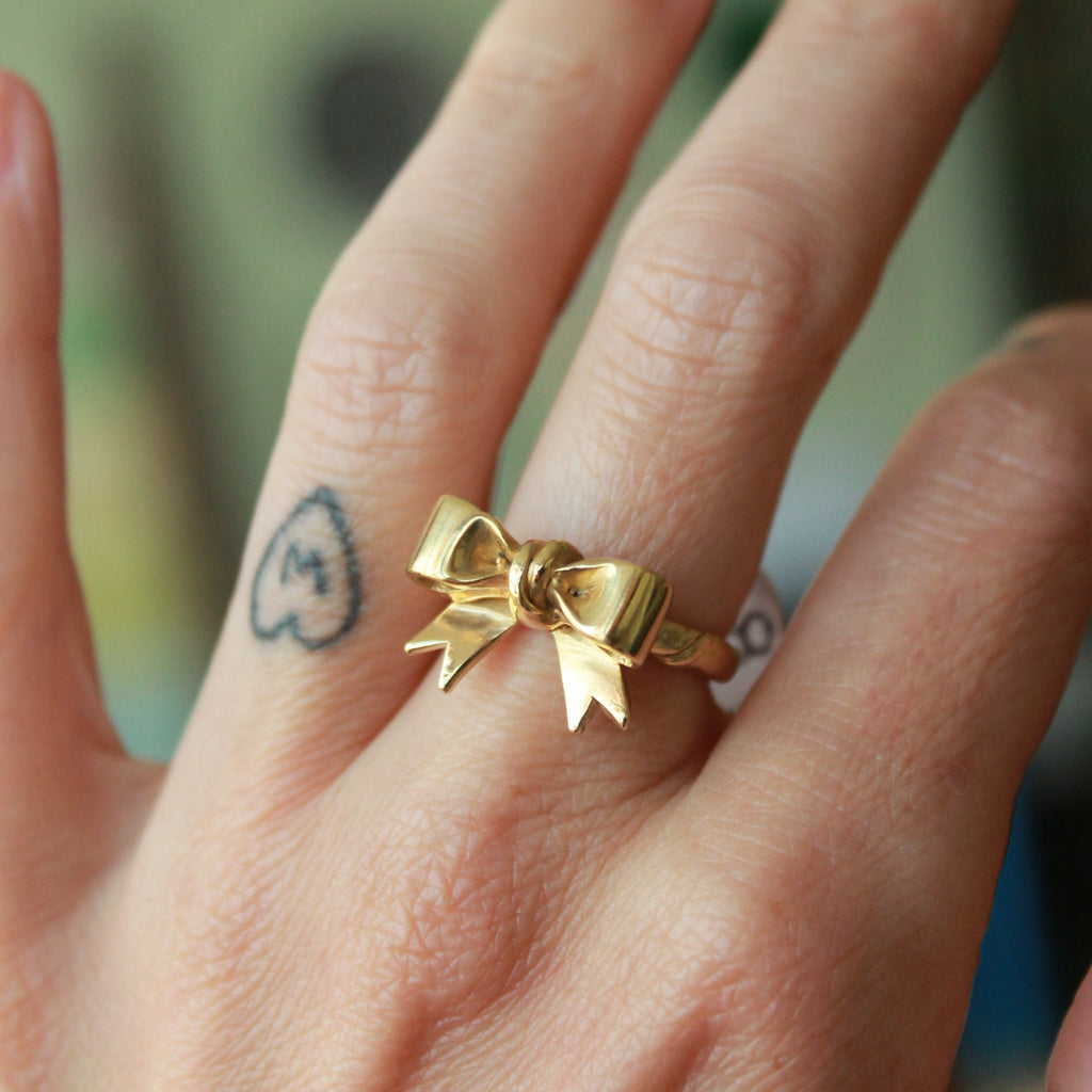 Gold bow-shaped ring on a finger with a blurred background
