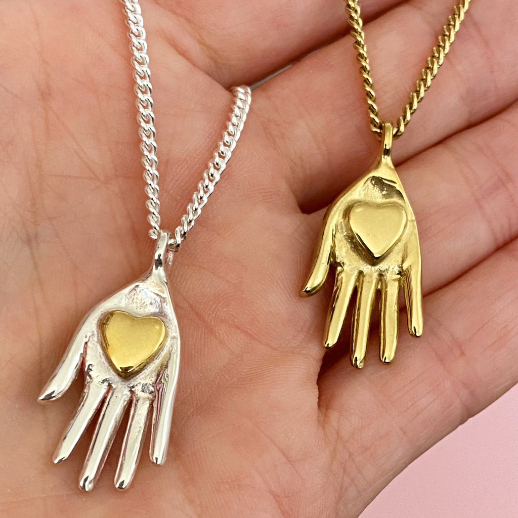 silver hand necklace with a gold heart in it's palm